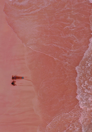 Pink beach with a woman and a child sitting on the shore.