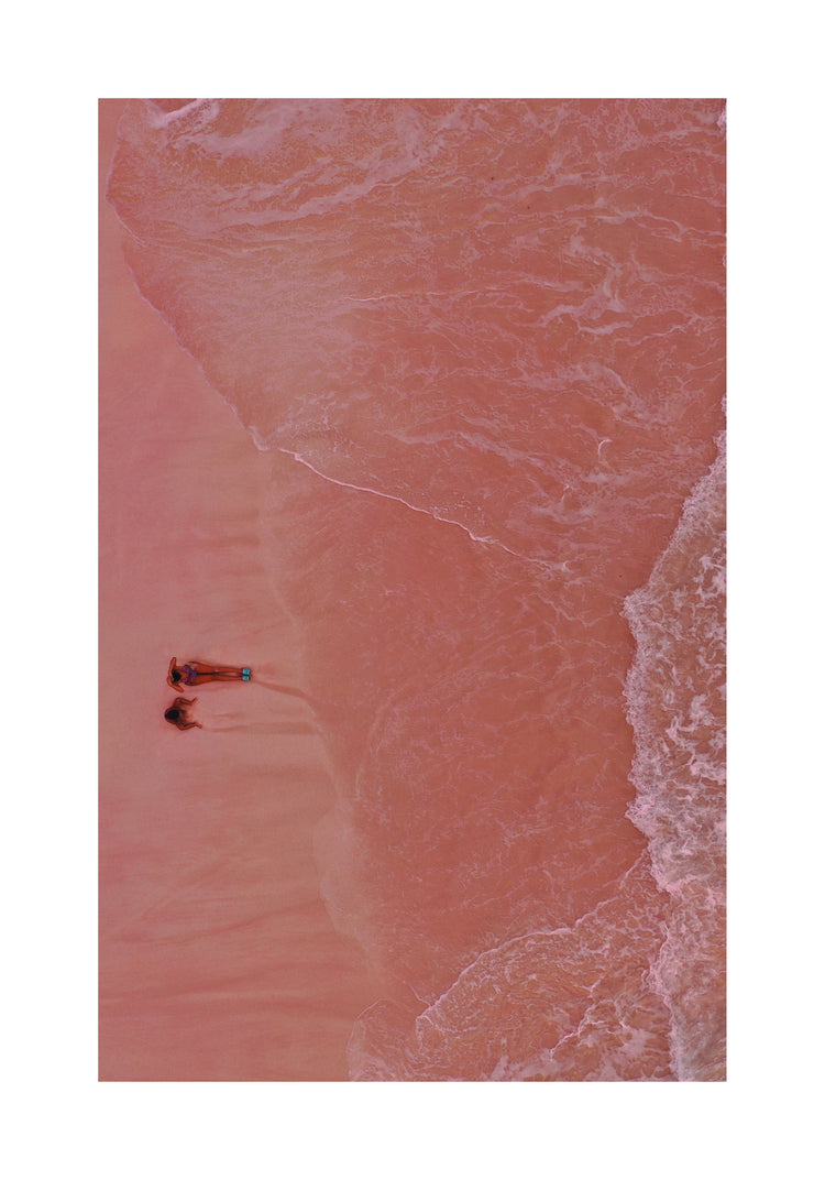 Pink beach with a woman and a child sitting on the shore.