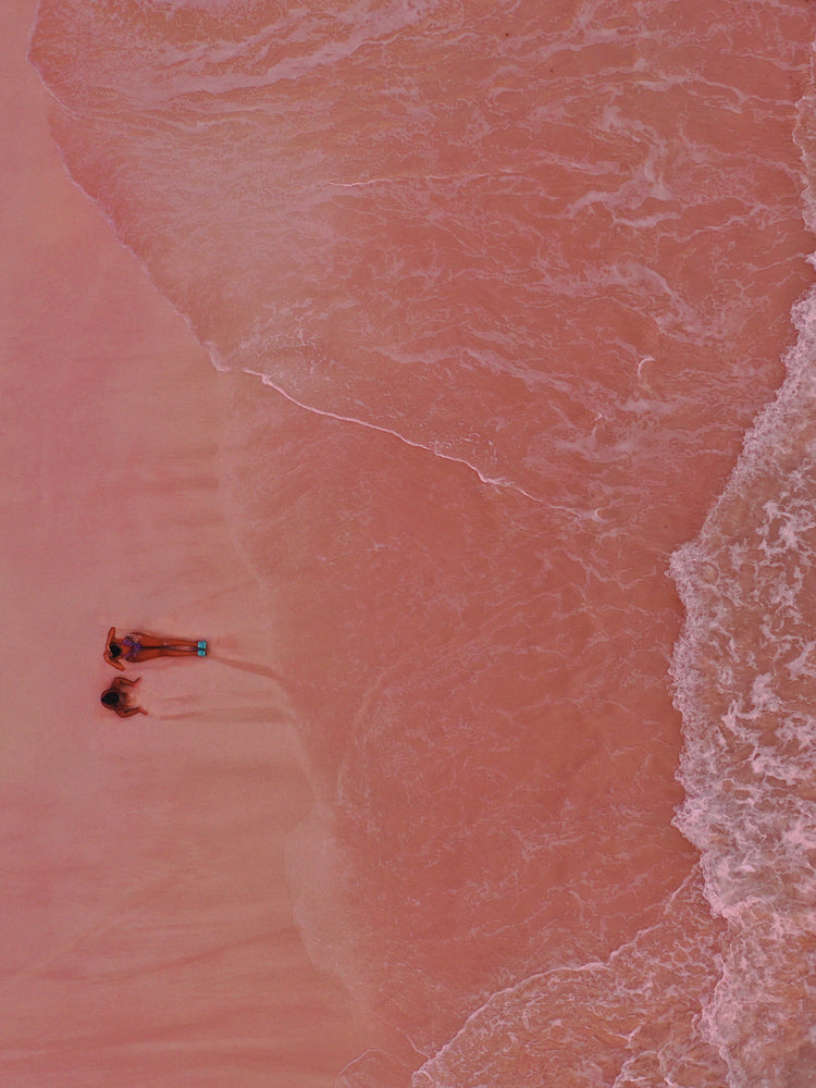 Pink beach with a woman and a child sitting on the shore.