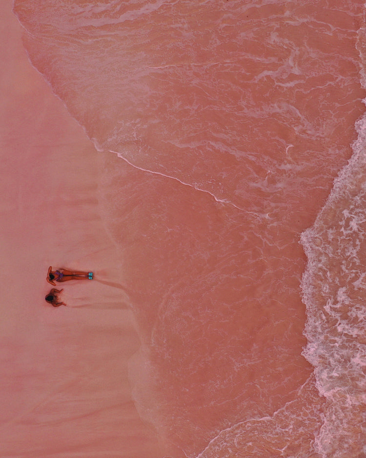 Pink beach with a woman and a child sitting on the shore.