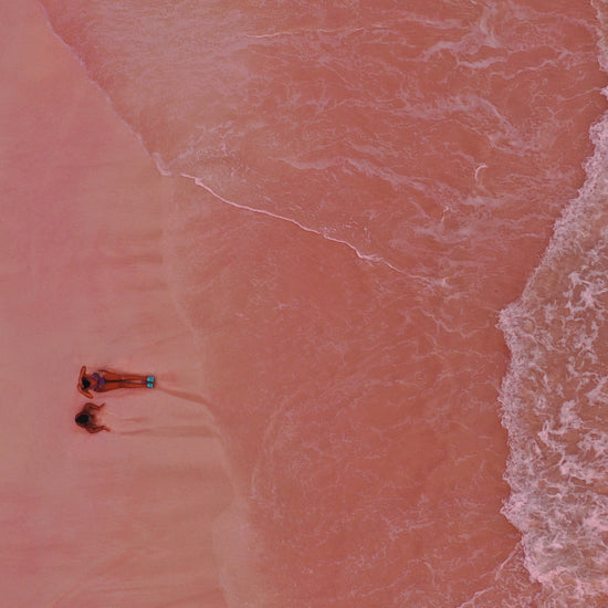 Pink beach with a woman and a child sitting on the shore.