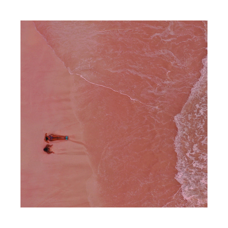 Pink beach with a woman and a child sitting on the shore.