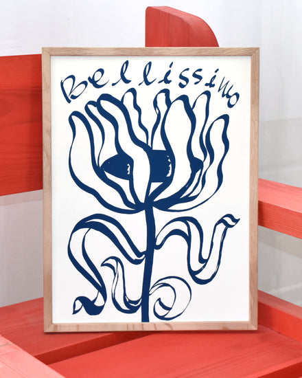 Framed poster with an illustration of a blue flower with the text Bellissimo is propped against a red chair. Illustration created by the artist Manne Jalilian.