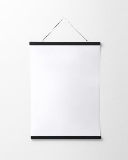 A blank white poster hangs on a plain white wall, elegantly secured by the Poster hanger Black, which features discreet magnets and two thin black bars for a sleek finish.