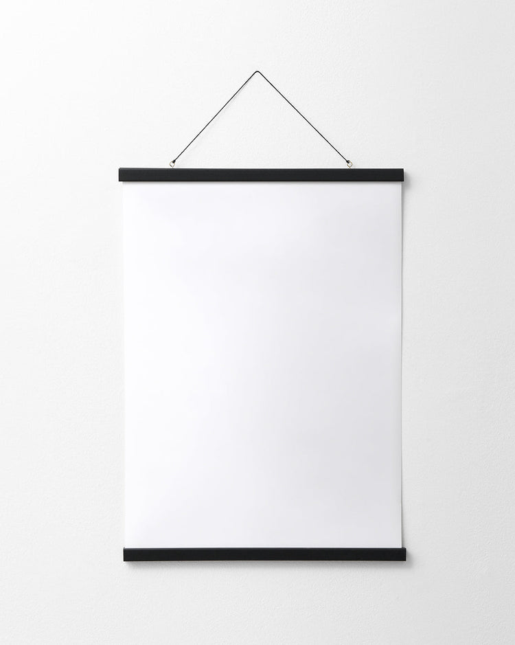A blank white poster hangs on a plain white wall, elegantly secured by the Poster hanger Black, which features discreet magnets and two thin black bars for a sleek finish.