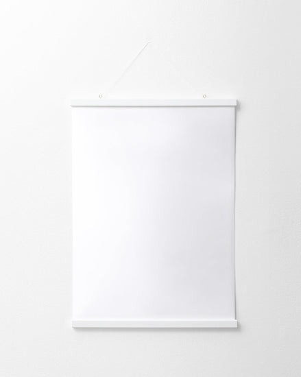 The Poster hanger White elegantly displays a blank white poster on a white wall. It features thin solid pine strips at the top and bottom, suspended by a string from two small nails, enhancing its minimalist charm.