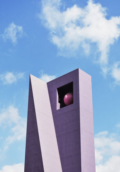 A tall, angular, purple structure set against a blue sky with clouds stands majestically like the Pershing Square Tower Poster. The building has a triangular peak and a square opening near the top, partially revealing a large red sphere within.