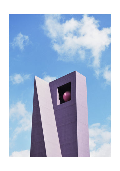 The Pershing Square Tower Poster depicts a tall, angular purple structure against a blue sky with white clouds, offering an architectural marvel. A large square opening near the top houses a pink sphere, and the buildings sharp lines contrast beautifully with the soft sky.