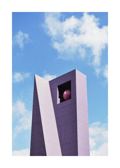 The Pershing Square Tower Poster showcases a tall purple geometric structure holding a red sphere, with a large square opening near the top. Its bold modern design contrasts against a bright blue sky with white clouds, capturing Hanna KLs imaginative essence.