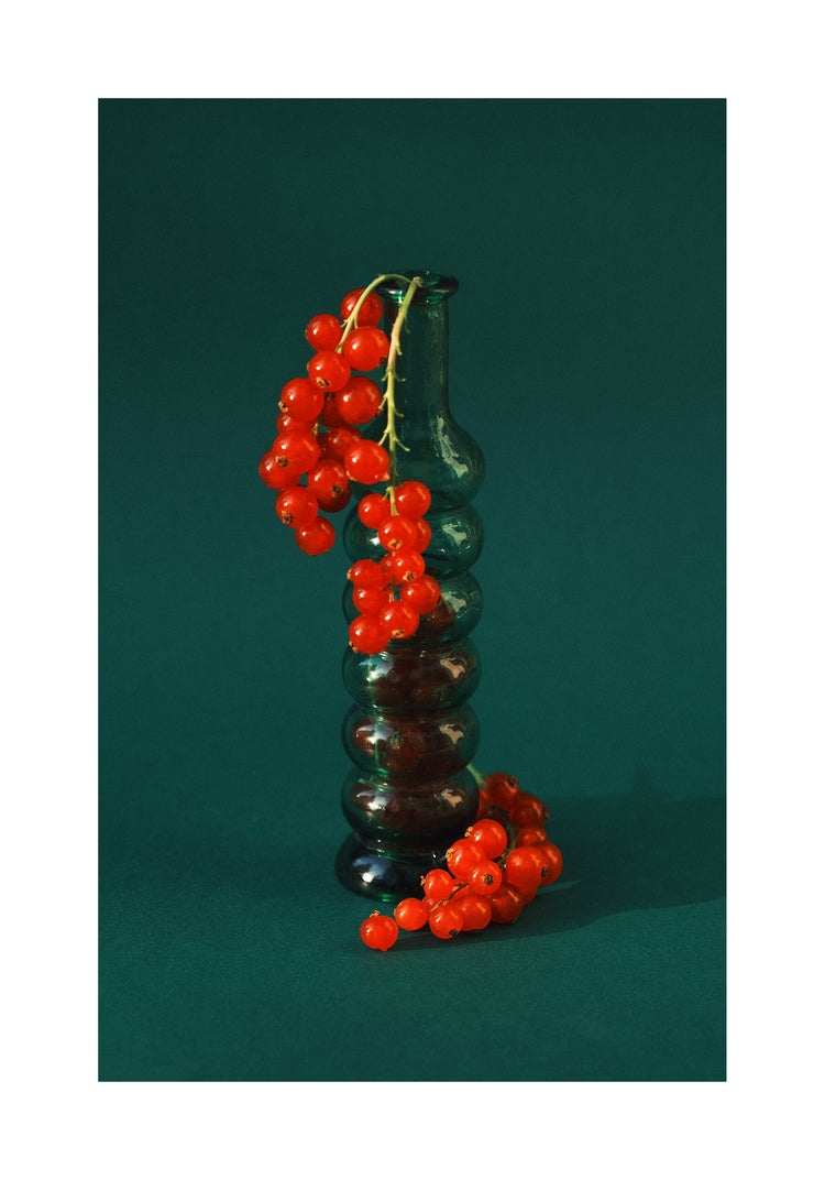 Green glass vase filled with redcurrant berries.