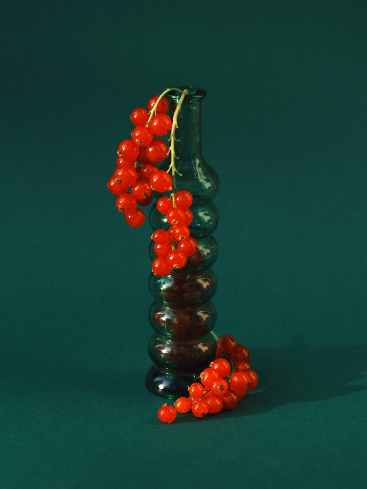 Green glass vase filled with redcurrant berries.