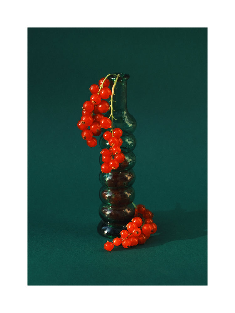 Green glass vase filled with redcurrant berries.