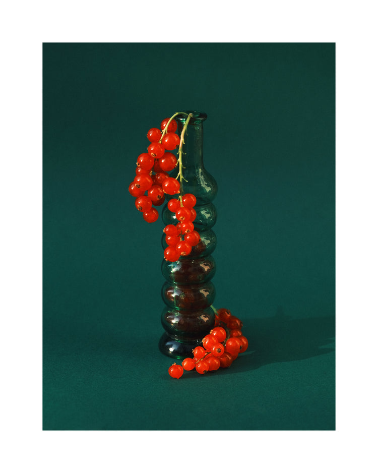 Green glass vase filled with redcurrant berries.
