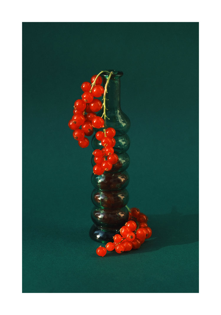 Green glass vase filled with redcurrant berries.
