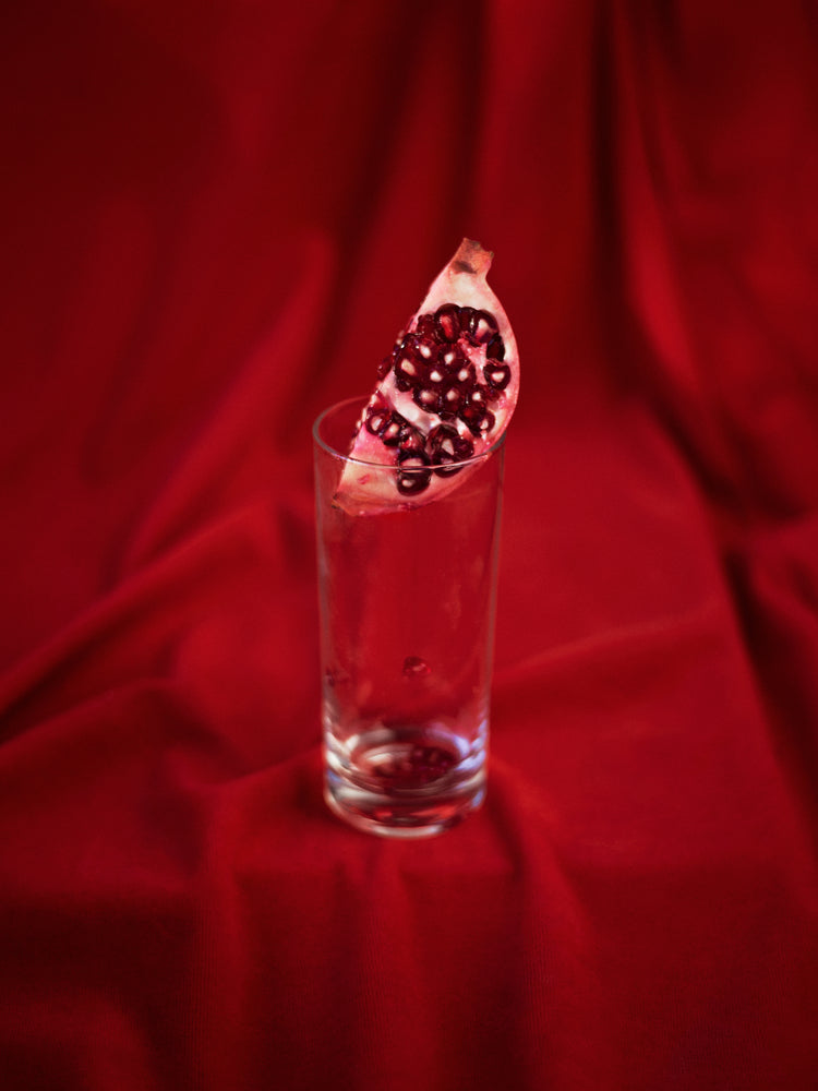 Slice of pomegranate in a glass standing on a blood red sheet.