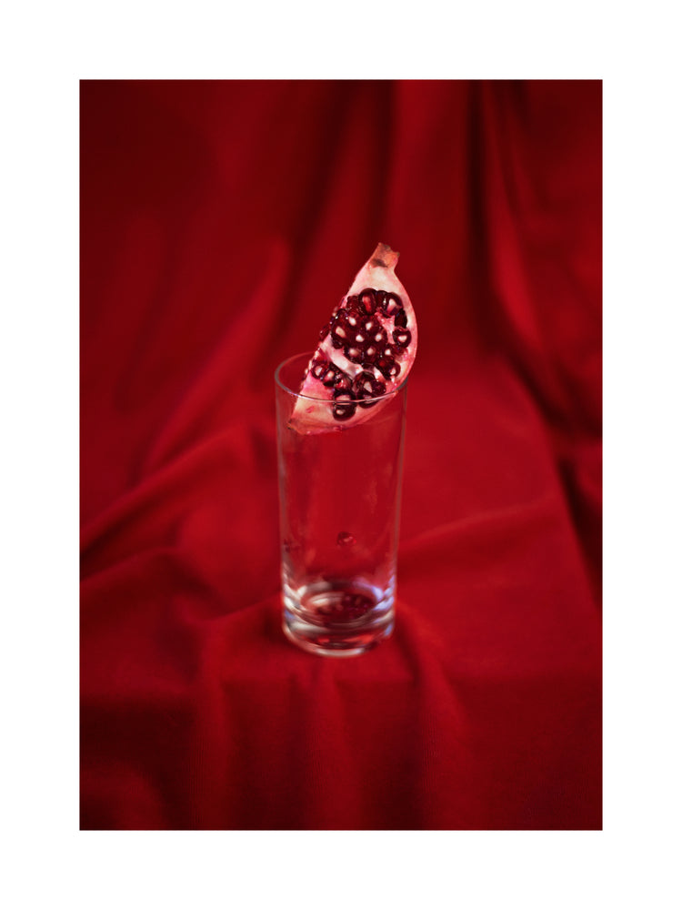 Slice of pomegranate in a glass standing on a blood red sheet.