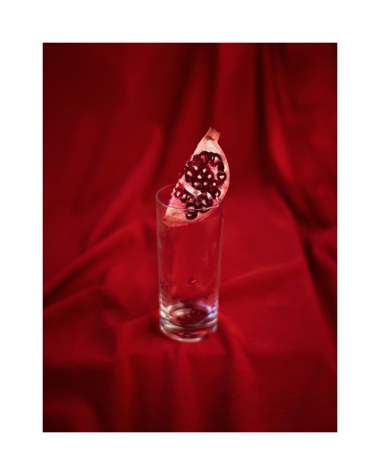 Slice of pomegranate in a glass standing on a blood red sheet.