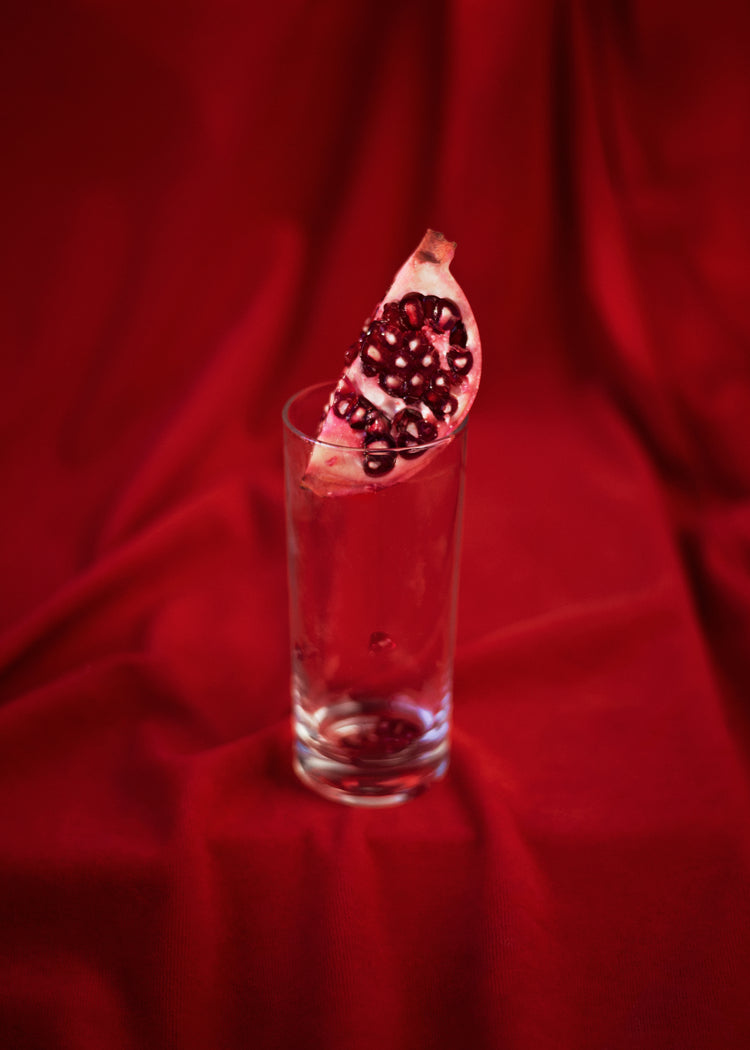 Slice of pomegranate in a glass standing on a blood red sheet.