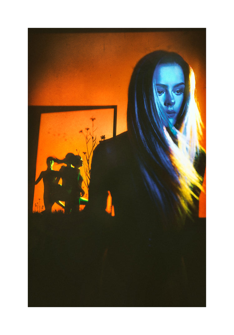 Woman with blonde hair and blue face standing in front of an orange wall.