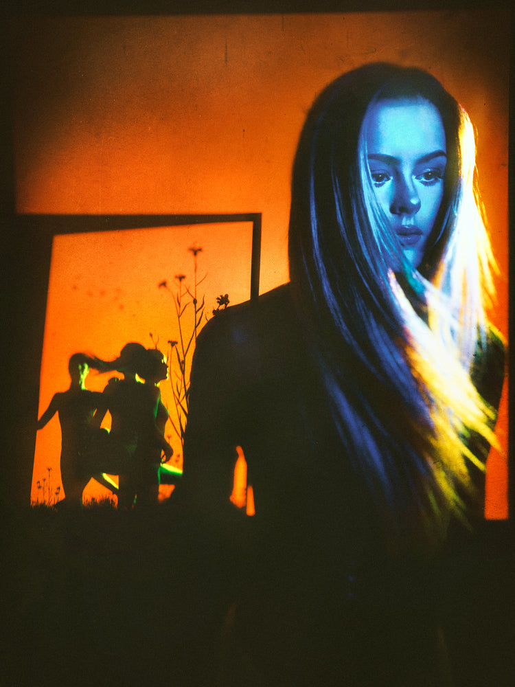 Woman with blonde hair and blue face standing in front of an orange wall.
