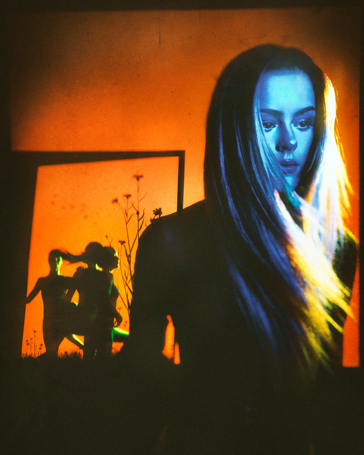 Woman with blonde hair and blue face standing in front of an orange wall.