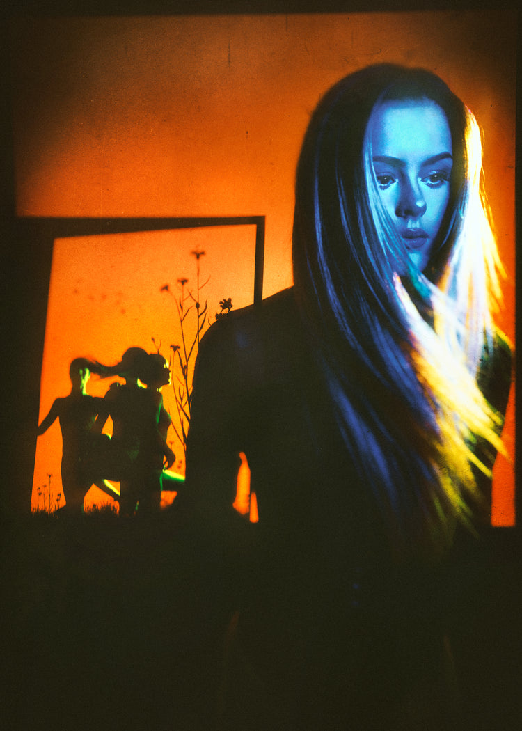 Woman with blonde hair and blue face standing in front of an orange wall.