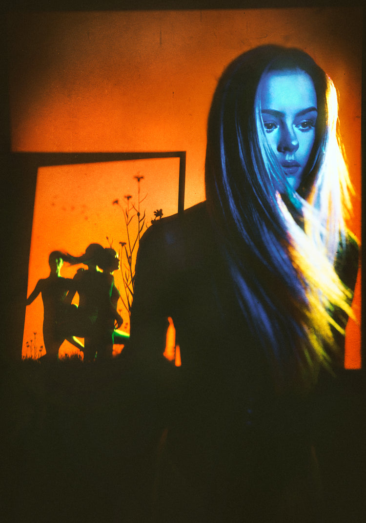 Woman with blonde hair and blue face standing in front of an orange wall.