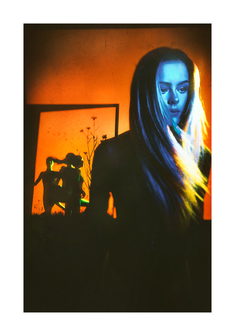 Woman with blonde hair and blue face standing in front of an orange wall.