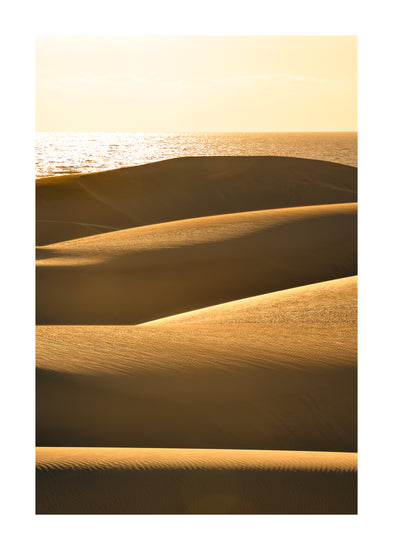 Sand dunes and a calm sea sparkling like gold.