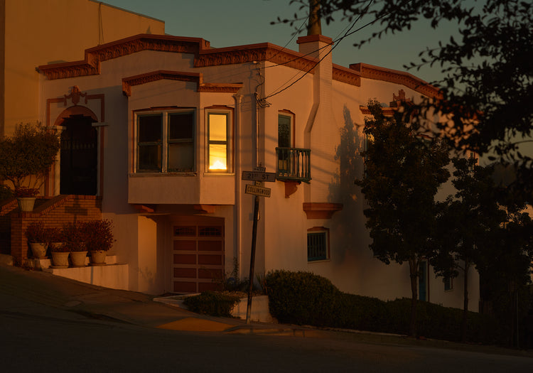 Suburban house laying at an intersection photographed during sunset.