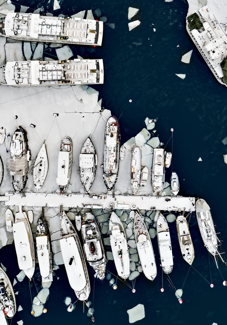 Cargo ship laying white on a dark sea covered in cracked ice.