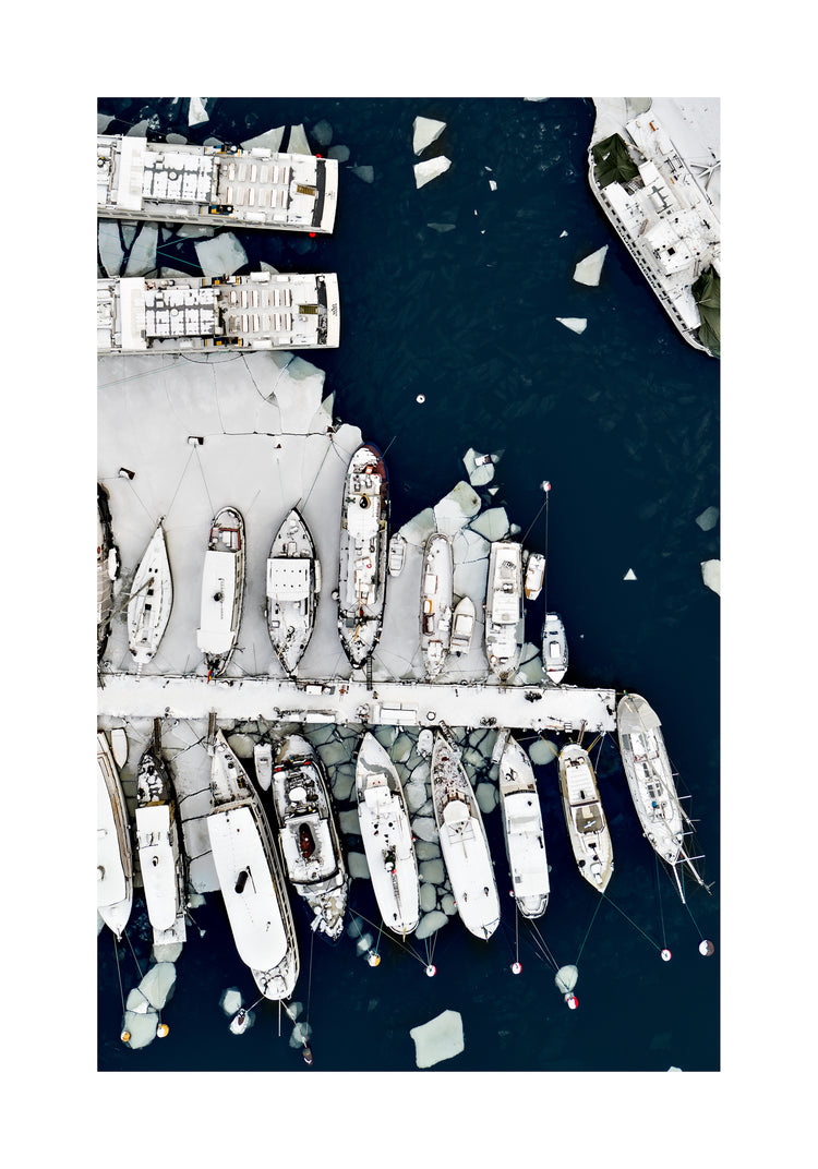 Cargo ship laying white on a dark sea covered in cracked ice.