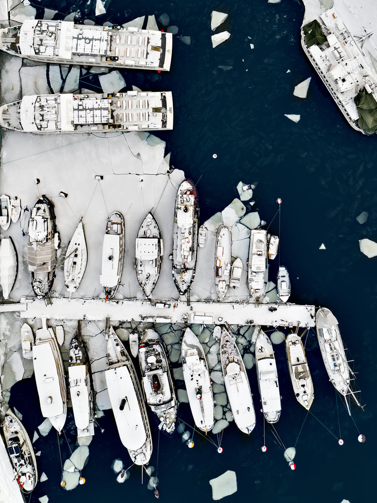 Cargo ship laying white on a dark sea covered in cracked ice.