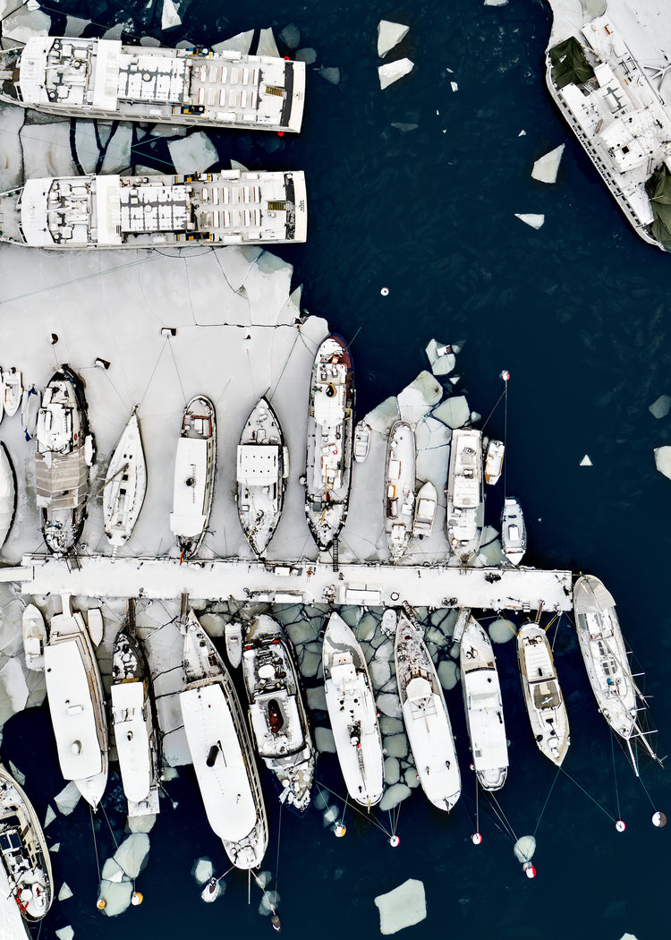 Cargo ship laying white on a dark sea covered in cracked ice.