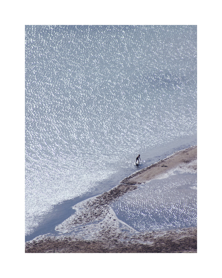Boy playing in the shallows of a big sea that is sparkling in the sunlight.