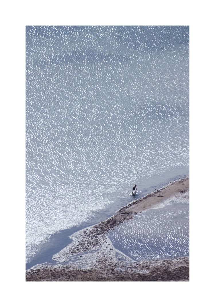 Boy playing in the shallows of a big sea that is sparkling in the sunlight.