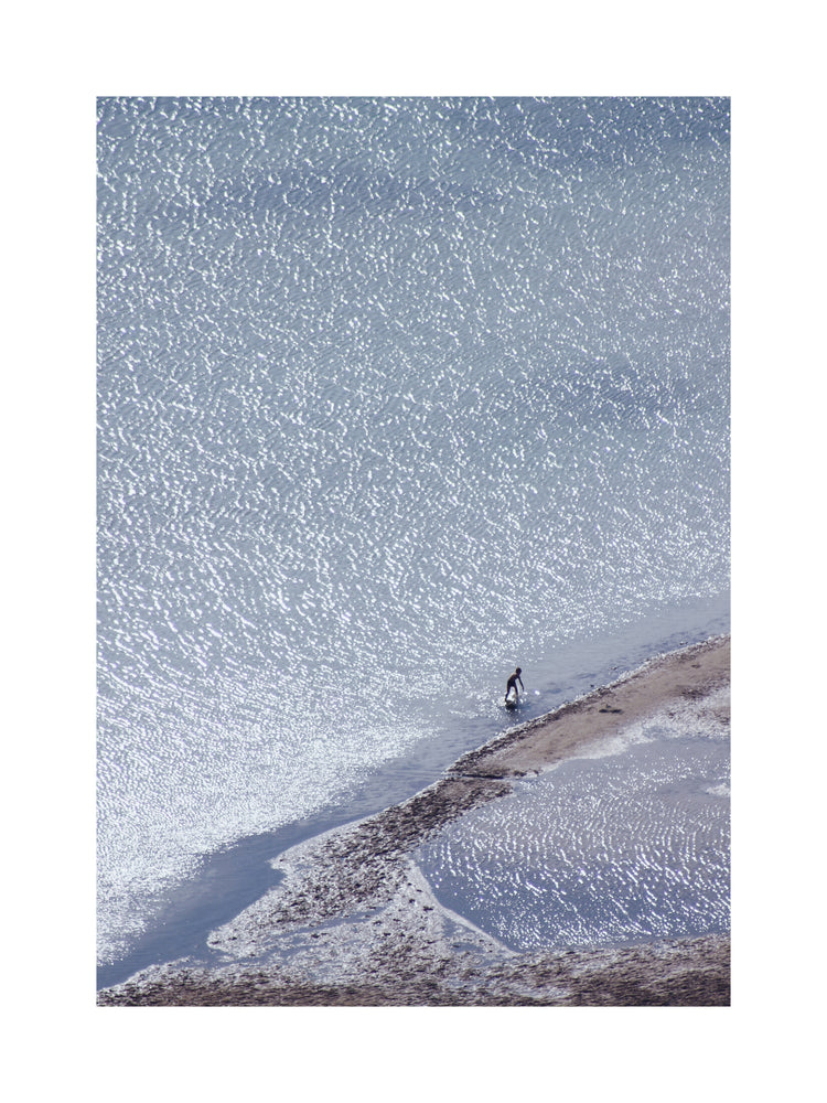 Boy playing in the shallows of a big sea that is sparkling in the sunlight.