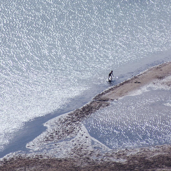 Boy playing in the shallows of a big sea that is sparkling in the sunlight.