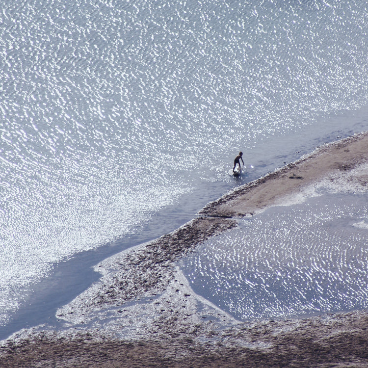 Boy playing in the shallows of a big sea that is sparkling in the sunlight.