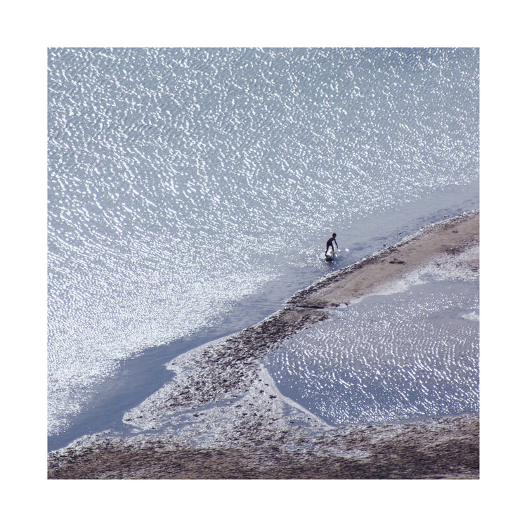 Boy playing in the shallows of a big sea that is sparkling in the sunlight.