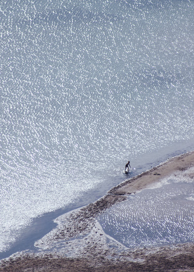 Boy playing in the shallows of a big sea that is sparkling in the sunlight.