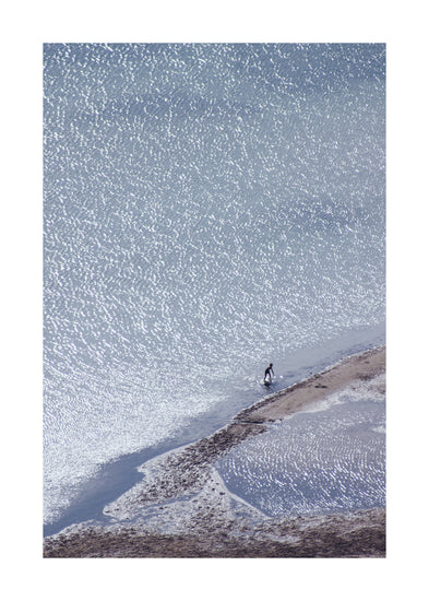 Boy playing in the shallows of a big sea that is sparkling in the sunlight.