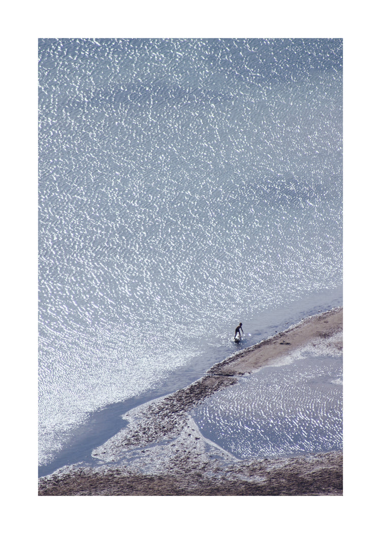 Boy playing in the shallows of a big sea that is sparkling in the sunlight.