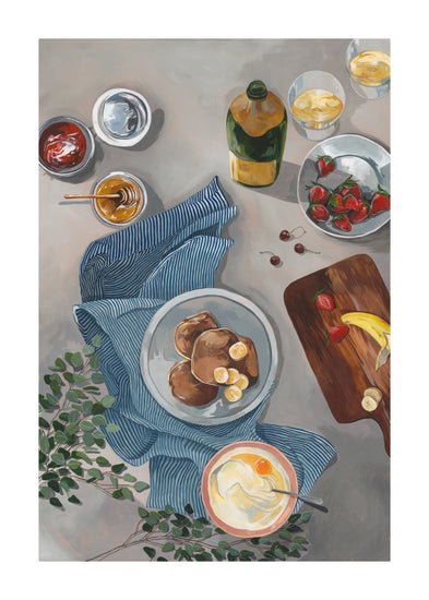 The Breakfast of Champions poster showcases fluffy pancakes topped with banana slices on a blue-striped cloth, a cutting board with cherries and strawberries, sparkling champagne in clear glasses, a yogurt bowl, and green leaves.