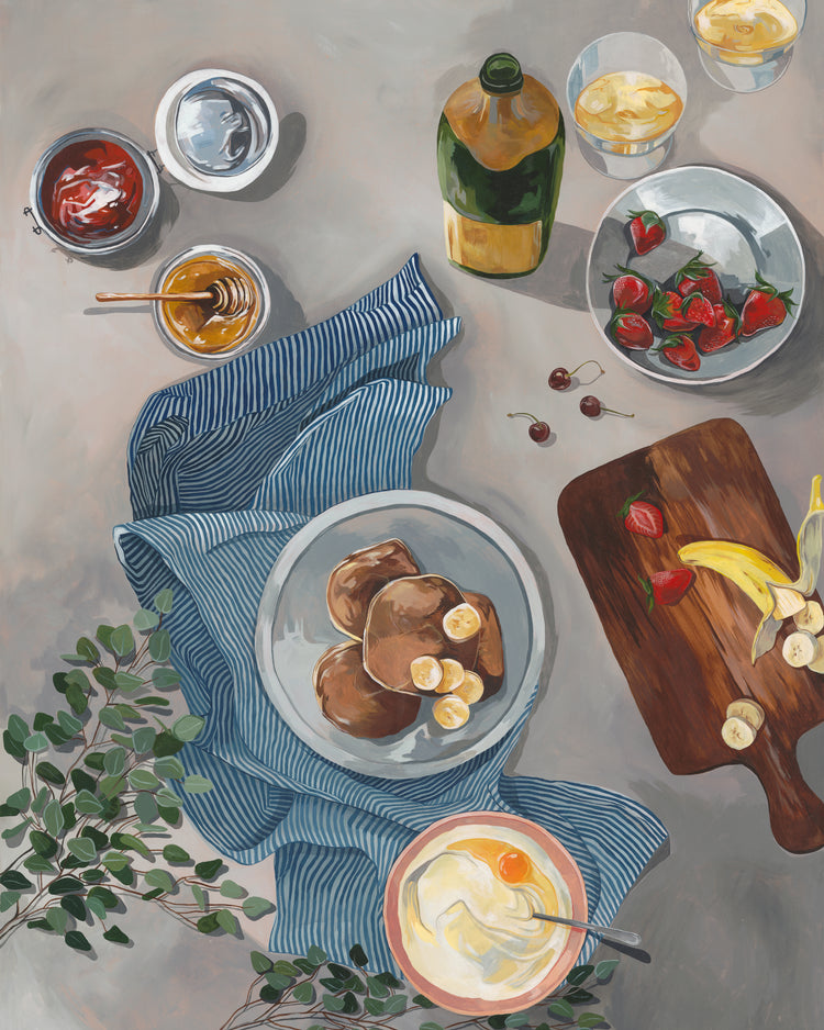 The Breakfast of Champions Poster captures a delightful morning spread of fluffy pancakes with banana slices, yogurt with fruit, strawberries on a cutting board, honey, jam, and assorted drinks. A blue-striped cloth and green leaves complete this inviting scene.