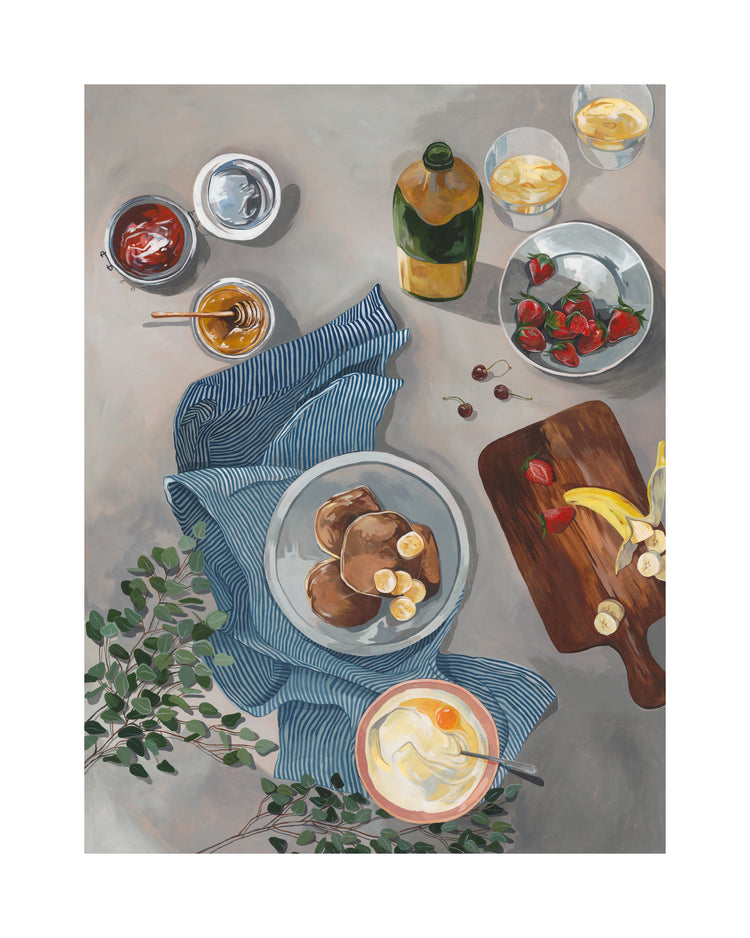 The Breakfast of Champions Poster depicts a delightful scene with fluffy pancakes, bananas on a striped cloth, a wooden board filled with more bananas and strawberries, along with yogurt, marmalade, honey, olive oil, and greenery for a fresh touch.