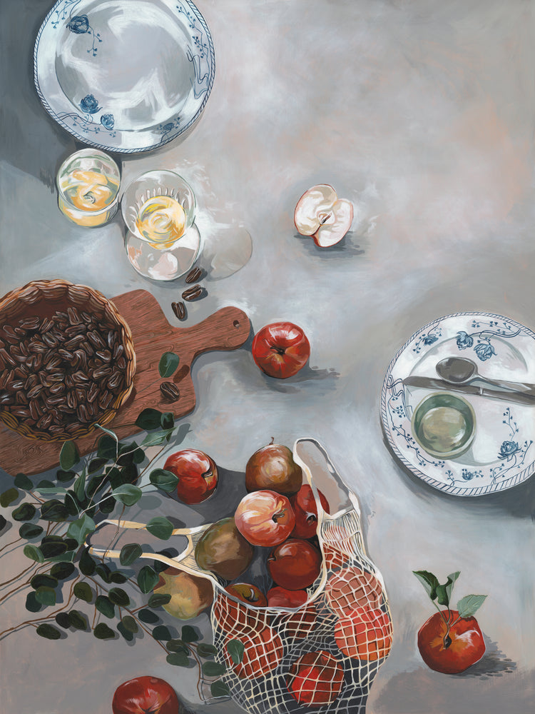 The How Do You Like These Apples Poster depicts a still life of a kitchen table with red apples, a mesh bag, pecans on a wooden board, plates with utensils, glasses of light beverage, and eucalyptus branches scattered across the textured surface for warm decor.