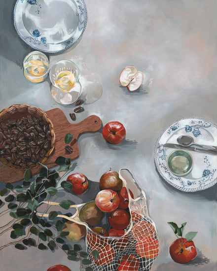 The How Do You Like These Apples Poster showcases a still life with red apples in a net bag on a kitchen table, accompanied by nuts on a wooden board, sliced apples, two decorative plates with cutlery, two glasses garnished with lemon, and a sprig of greenery adding warmth to the scene.