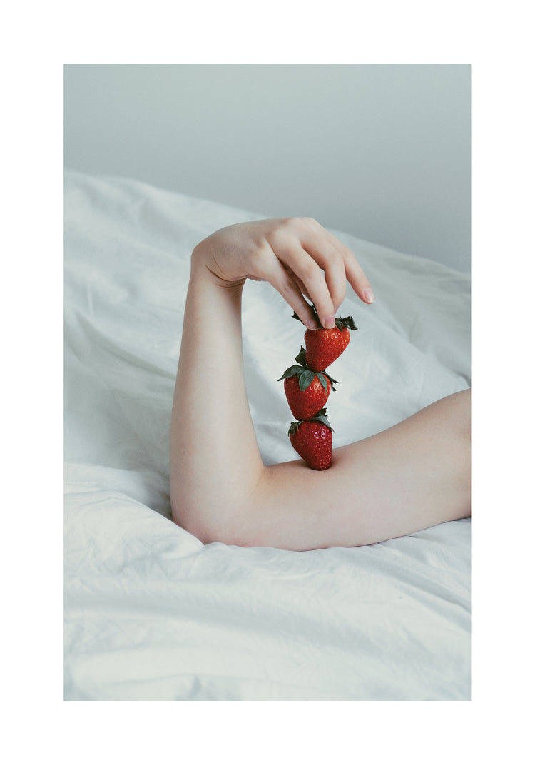 Female arm resting on a sheet with three strawberries stacked on her skin.