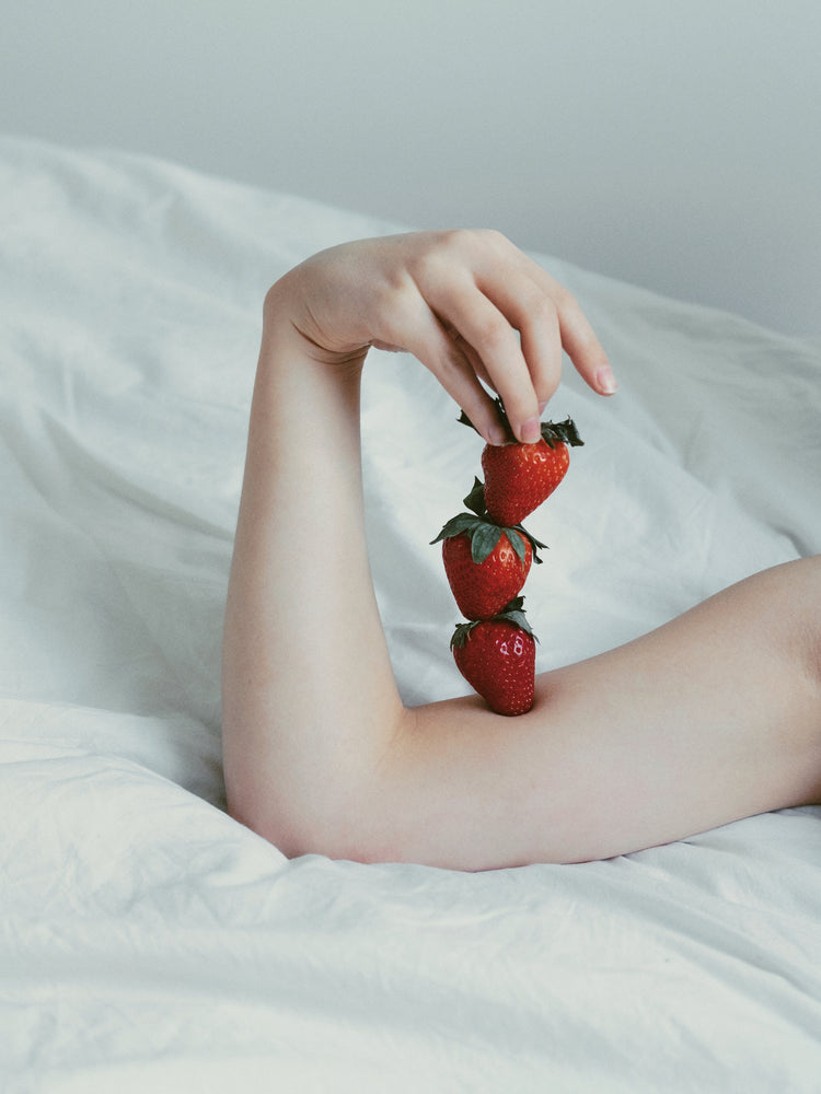 Female arm resting on a sheet with three strawberries stacked on her skin.